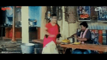 a woman in a red sari is standing in front of a table while another woman stands behind her .