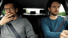 two men are sitting in the back seat of a car . one of the men is wearing glasses .