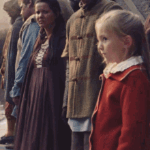 a girl in a red jacket stands in front of a group of people with the word sky visible in the background