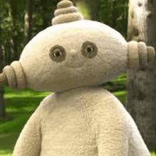 a stuffed animal is standing in the grass in the woods .