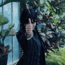 a woman in a black jacket is giving a thumbs up sign in a greenhouse .