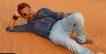 a man wearing sunglasses is laying on the ground in the desert