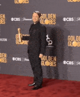 a man in a suit is dancing on a red carpet in front of a wall that says golden globes