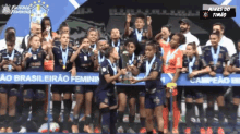 a group of female soccer players are holding a trophy in front of a banner that says minas do timão