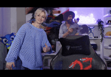 a woman in a blue sweater is giving a thumbs up in front of a secret lab chair