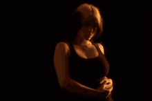 a woman in a black tank top is standing in the dark and holding her stomach .