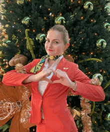 a woman in a red suit is making a heart shape with her hands in front of a christmas tree