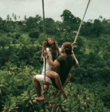 a man and woman are sitting on a swing in the air