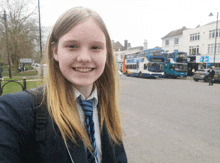 a girl in a school uniform is smiling in front of a double decker bus that says d