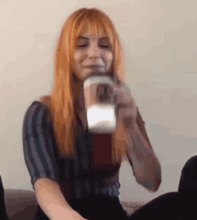 a woman with long red hair is sitting on a couch drinking from a cup .