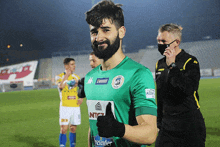 a soccer player wearing a green jersey that says ntc giving a thumbs up