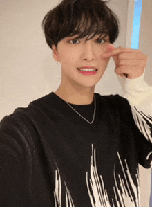 a young man wearing a black and white sweater and a necklace takes a selfie