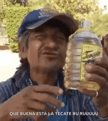 a man in a hat is holding a bottle of tecate and drinking from it .