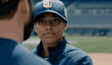 a man and a woman are standing next to each other on a baseball field . the woman is wearing a baseball cap .