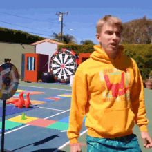 a man wearing a yellow hoodie with the letter w on it is standing in front of a large dart board