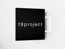 a black sign that says t8project is hanging on a white wall