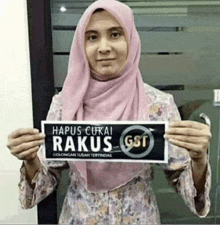 a woman in a pink hijab is holding up a sign that says " hapus cukai raku gst "