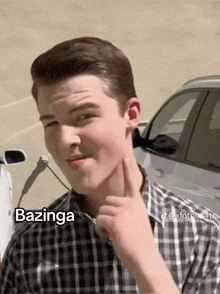 a young man in a plaid shirt is pointing to his ear and the word bazinga is on the bottom right