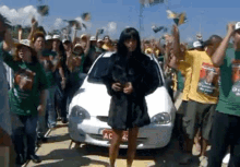 a woman in a black dress stands in front of a white car with a license plate that says ac