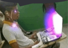 a boy is sitting in front of a laptop computer with a purple light coming out of it