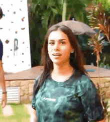 a woman in a green shirt is standing in front of a climbing wall and looking at the camera .