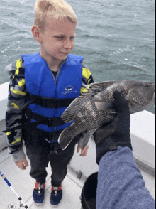 a boy wearing a life vest holds a fish