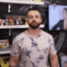 a man with a beard wearing a white shirt is standing in front of a shelf with toys on it .