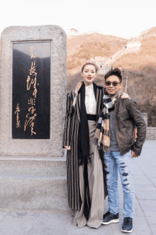 a woman stands next to a man in front of a stone plaque with chinese writing on it