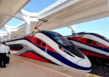 a red white and blue train is parked next to another train on a platform