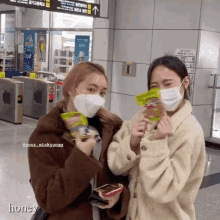 two women wearing face masks are standing next to each other and one of them is holding a bag of candy