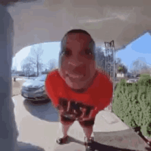 a man wearing a red shirt and shorts is standing in front of a doorbell .