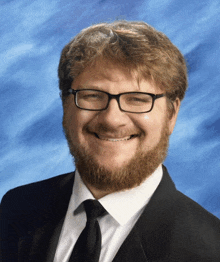 a man with glasses and a beard is smiling in front of a blue sky