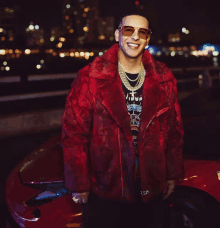 a man wearing a red fur coat and sunglasses is standing next to a red car