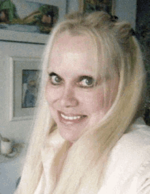 a woman with long blonde hair is smiling for the camera while wearing a white sweater .