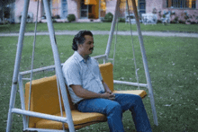 a man with a mustache sits on a swing in the grass