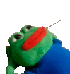 a green stuffed frog with a red face and a blue shirt is holding a stick in its mouth .