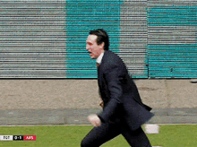 a man in a suit is running on a field with a scoreboard behind him that says tot 0-1 ars