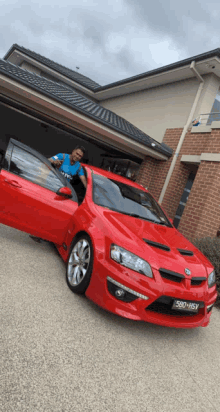 a man is standing next to a red car with a license plate that says 580-h5y