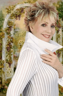 a woman in a striped shirt is smiling in front of a painting of grapes