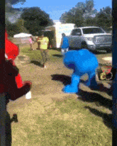 a group of people are standing in a field with a truck in the background and a blue monster in the foreground that says hot