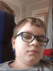 a young boy wearing glasses is sitting in a chair with his eyes closed