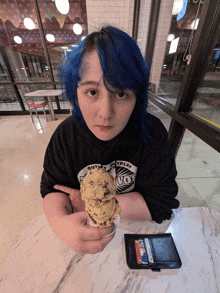 a girl with blue hair is sitting at a table holding an ice cream cone and wearing a black shirt that says outplay