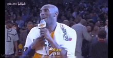 a man in a lakers jersey is holding a microphone in front of a crowd