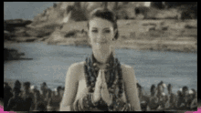 a woman is praying in front of a crowd of people while standing in front of a body of water .