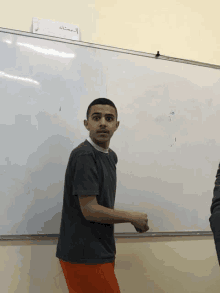 a young man stands in front of a whiteboard with arabic writing