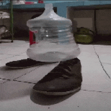 a bottle of water is sitting on top of a pair of shoes on a tiled floor .