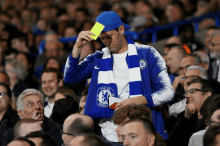 a man in a chelsea jacket is holding a yellow card in his hand .