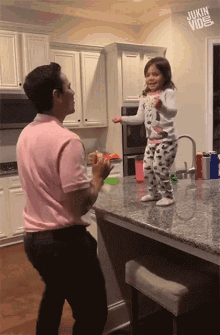 a man and a little girl are dancing in a kitchen and the girl is wearing a mickey mouse shirt