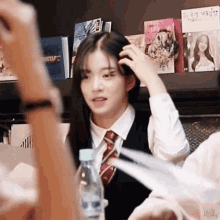 a girl in a school uniform adjusts her hair while sitting in front of a shelf with books on it