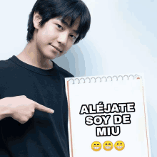 a young man pointing at a notepad that says alejate soy de miu